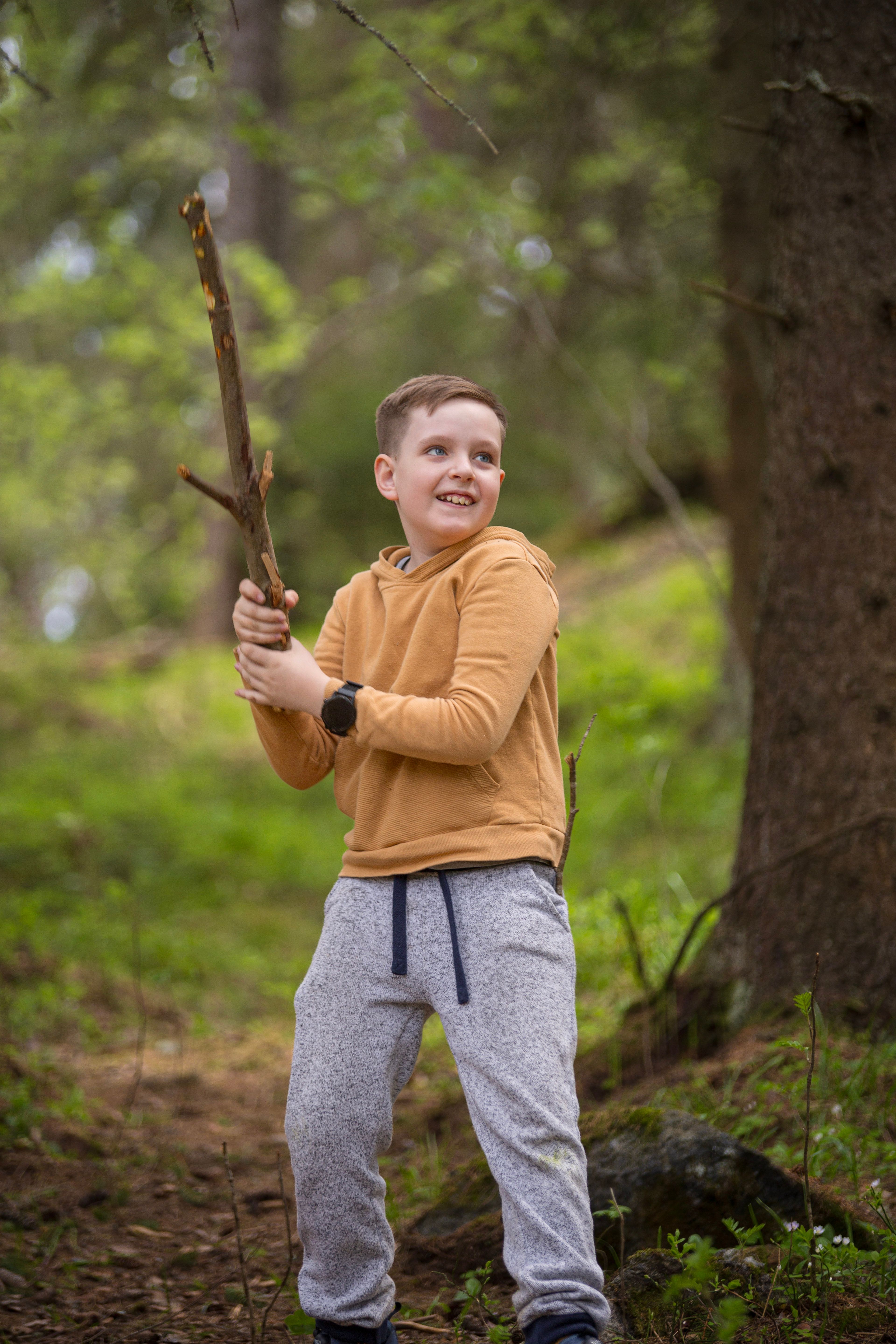 A joyful young boy with stick on a forest trail, embracing nature and fun.