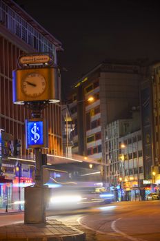 Vibrant urban night scene featuring a bustling street and a classic clock tower.