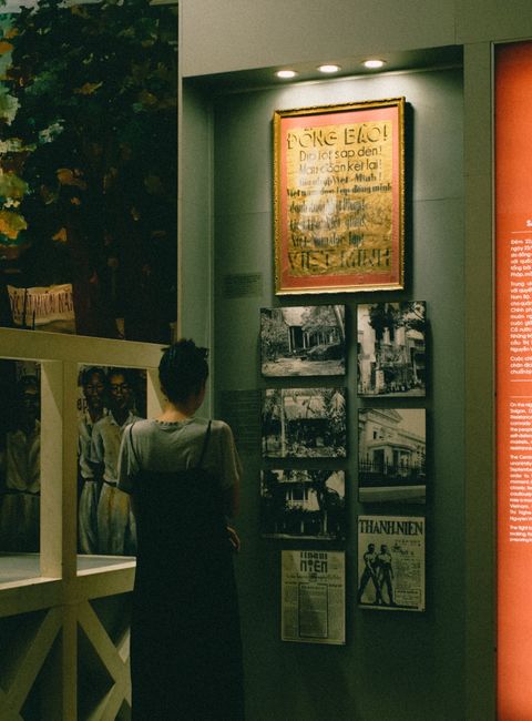 A woman with short hair stands in front of an art exhibit, observing historical posters and photos on a museum wall.