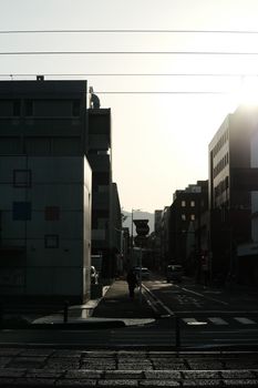 City street scene with silhouetted buildings and warm sunlight creating a dramatic urban atmosphere.