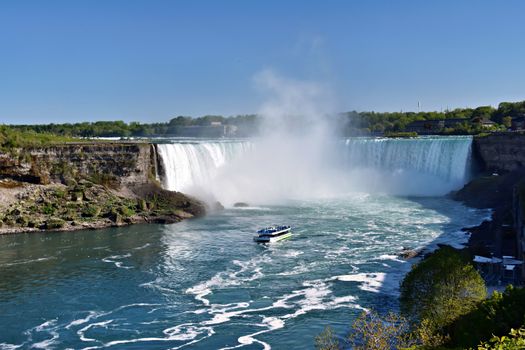 Dramatic scene of Niagara Falls with a tour boat navigating the misty waters.