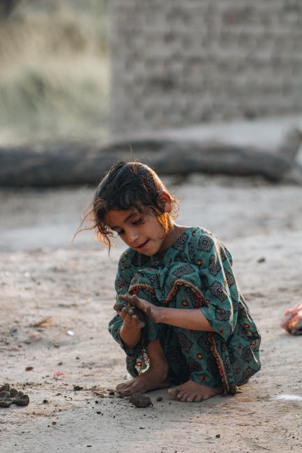 A young girl is playfully interacting with sand outdoors, capturing childhood innocence.