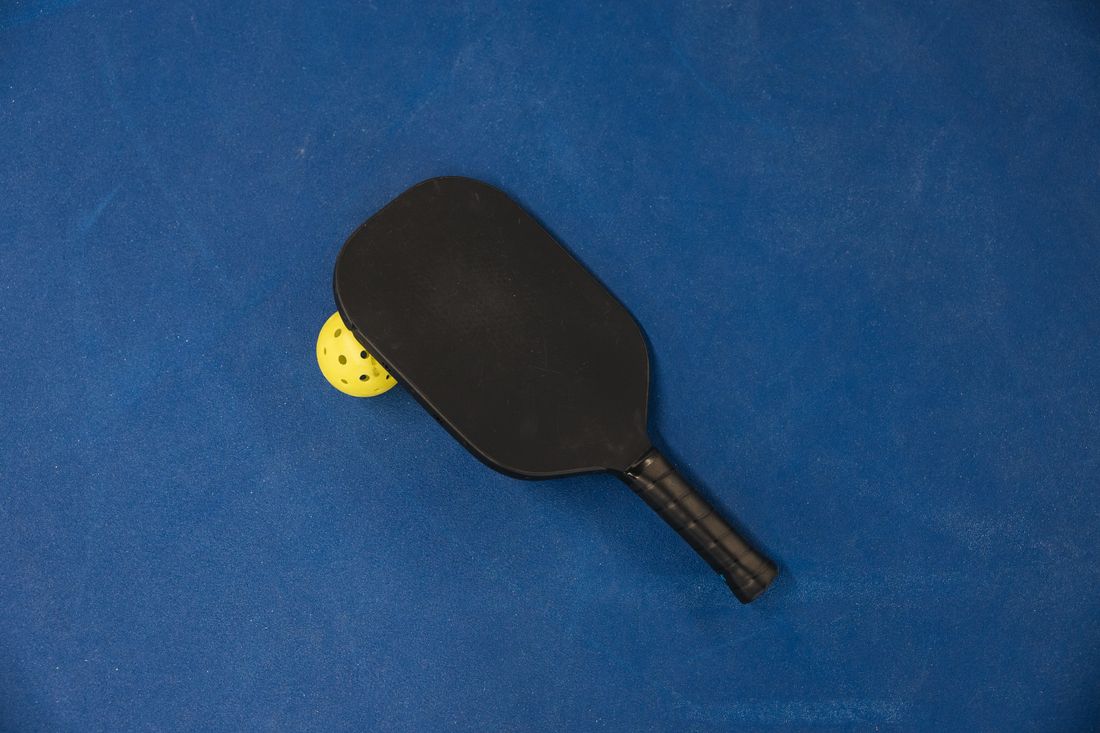 A pickleball paddle and yellow ball