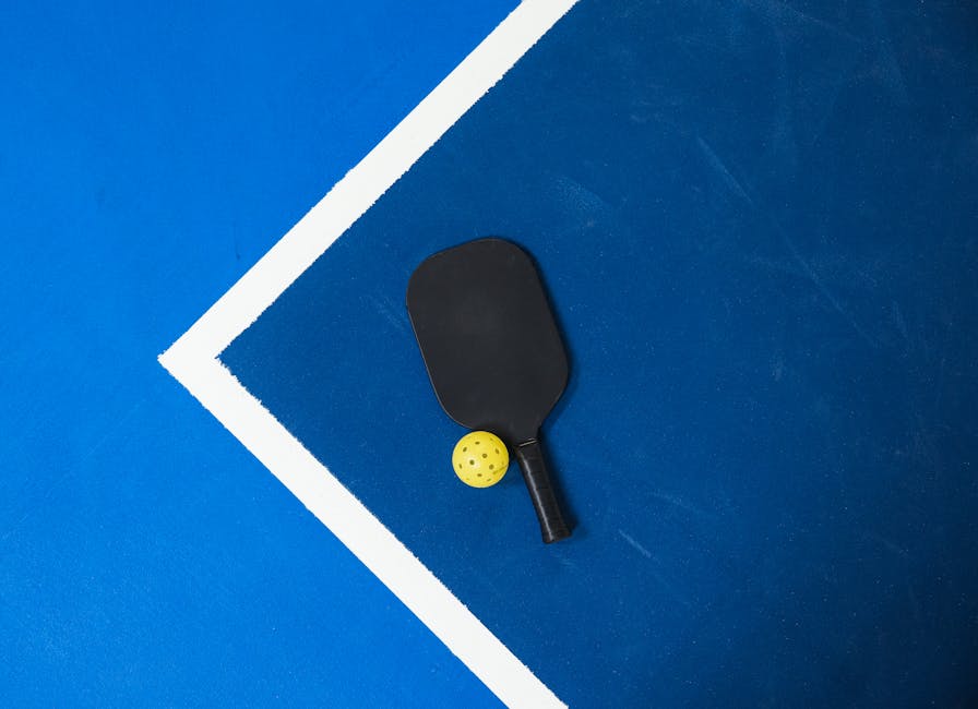 Close-up of a pickleball paddle and ball on a vibrant blue court surface showing geometric lines.