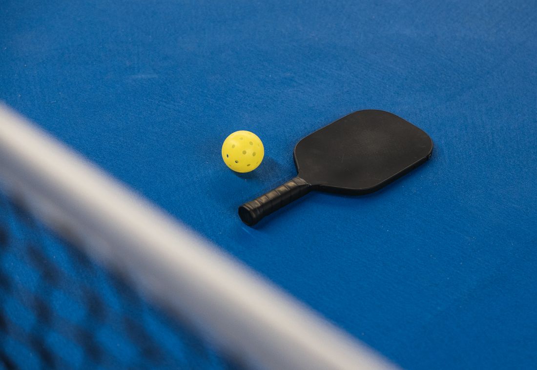 A pickleball paddle and ball resting on a blue court