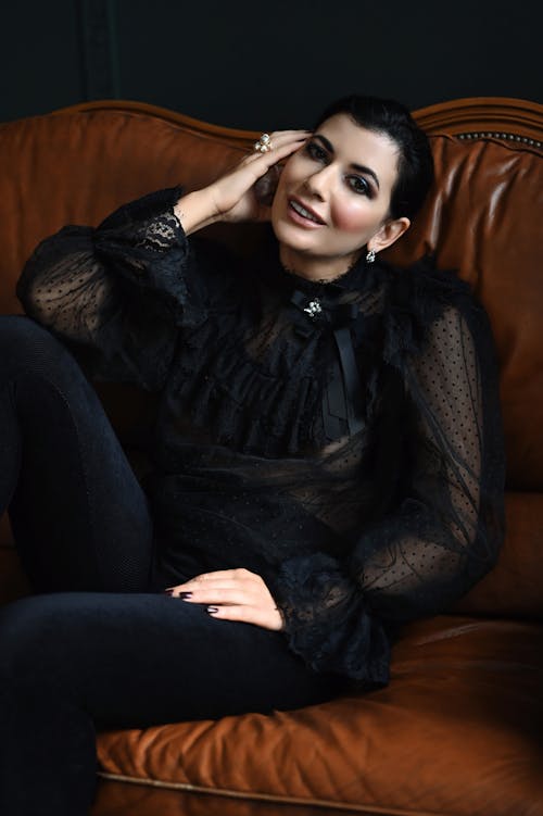 Brunette Wearing Elegant Black Clothing, Sitting on a Brown Leather Sofa