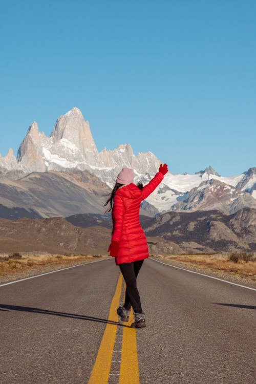 Woman in Red Jacket Standing on Road with Mountains behind