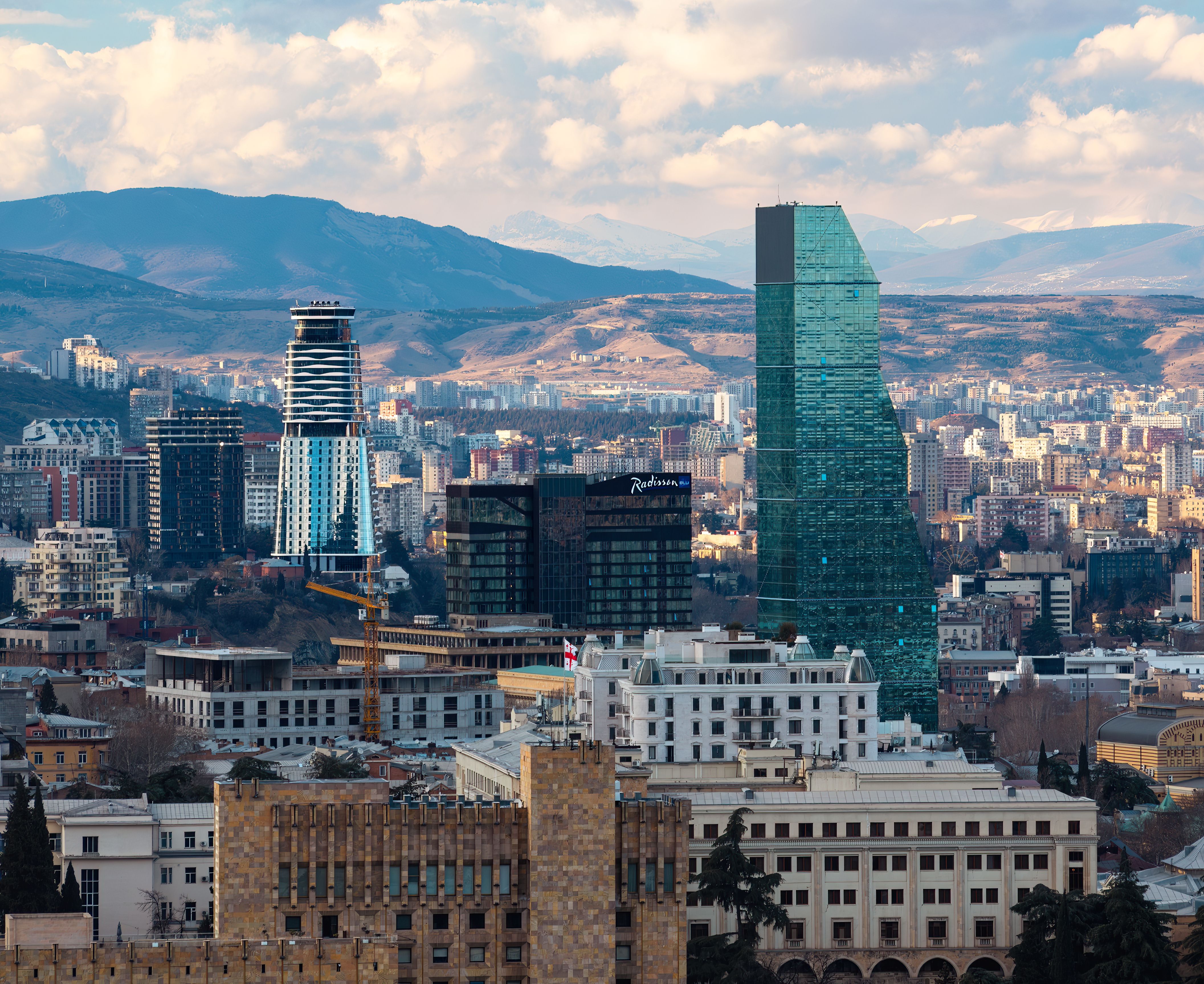A scenic view of Tbilisi's modern skyline with towering skyscrapers and mountain backdrop.