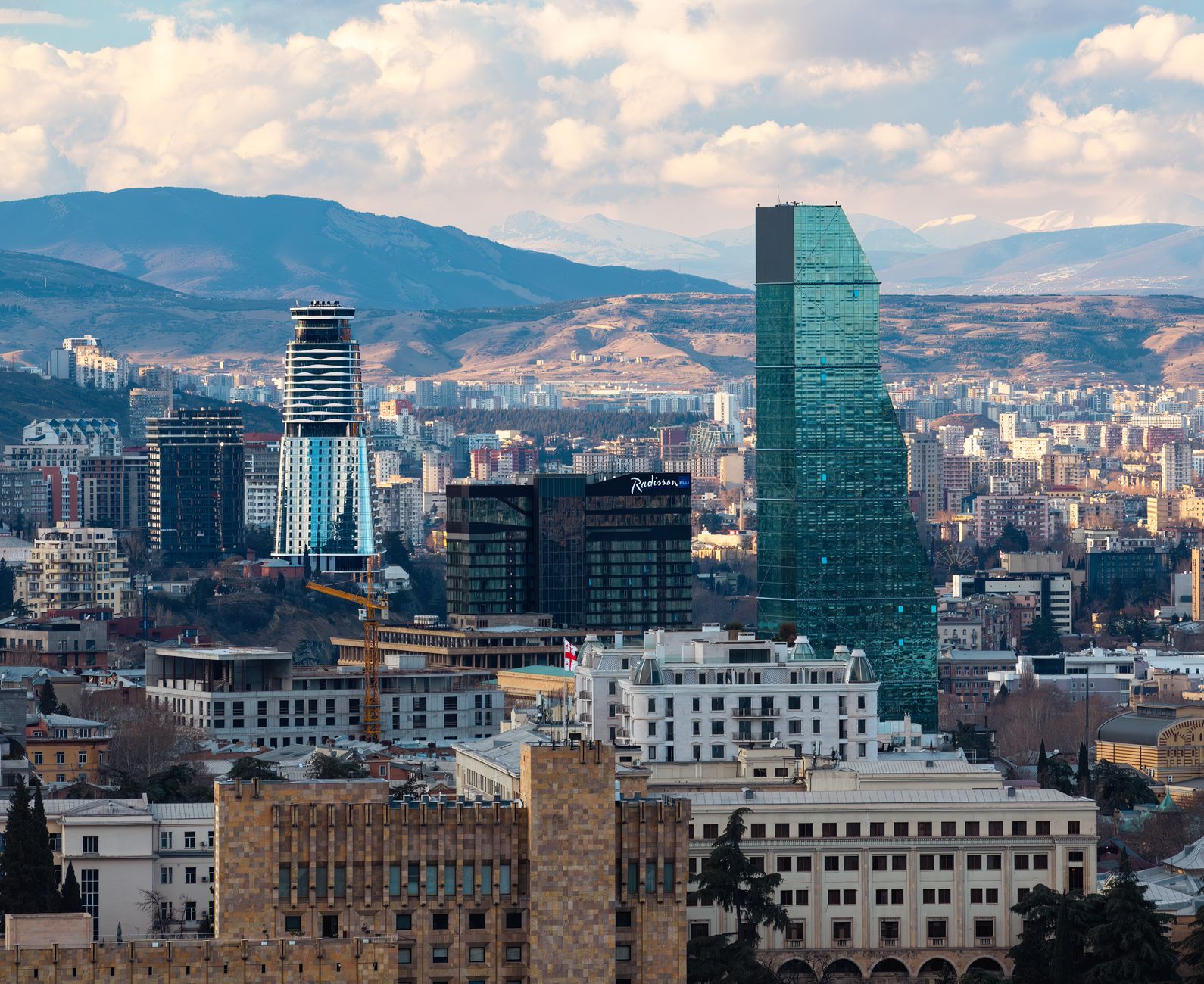 A scenic view of Tbilisi's modern skyline with towering skyscrapers and mountain backdrop.