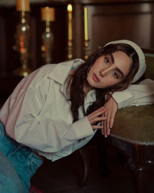 Free A fashionable young woman poses indoors wearing a white blouse and headband, creating a warm and artistic mood. Stock Photo