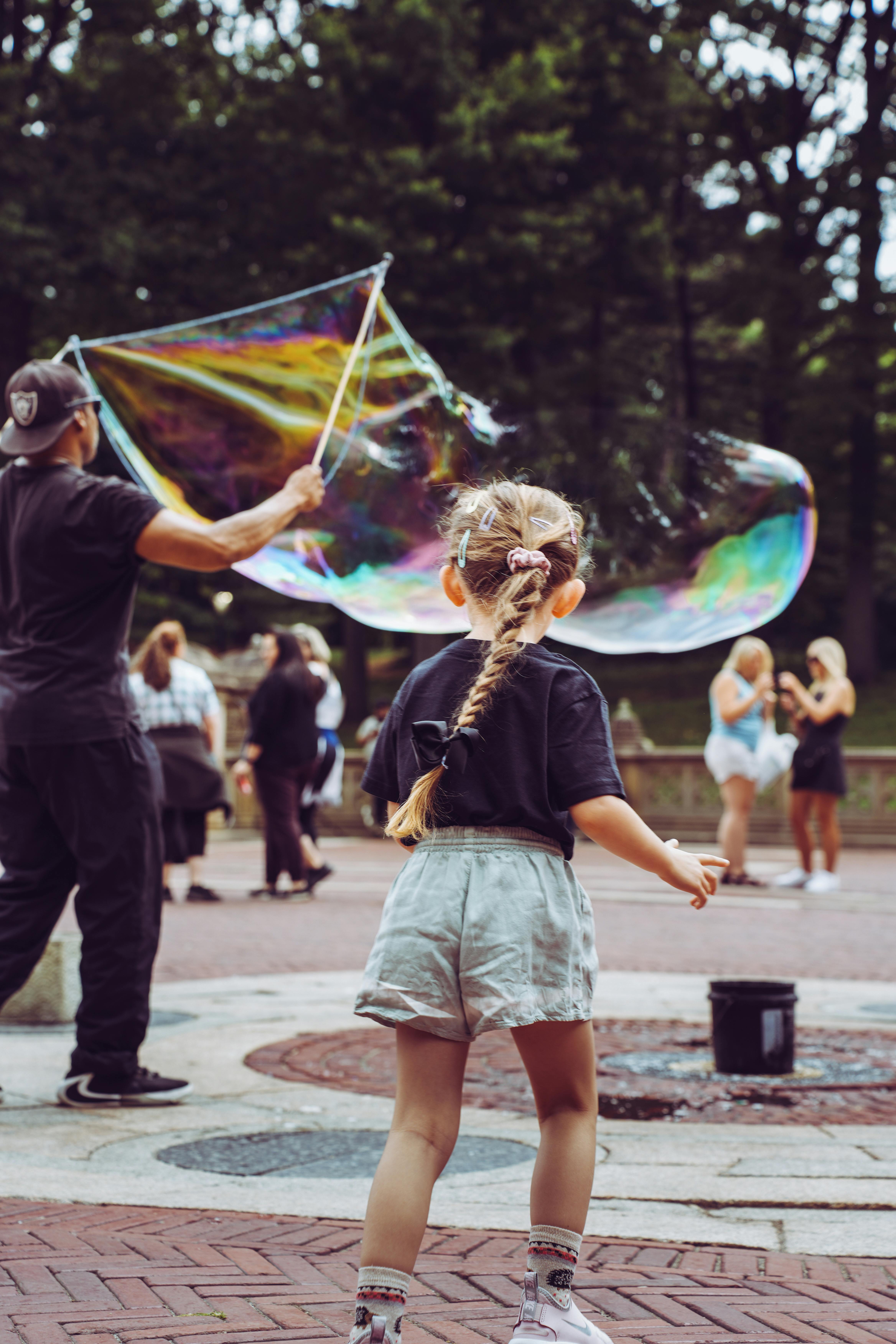 Little girl captivated by giant bubble activity in a vibrant park.