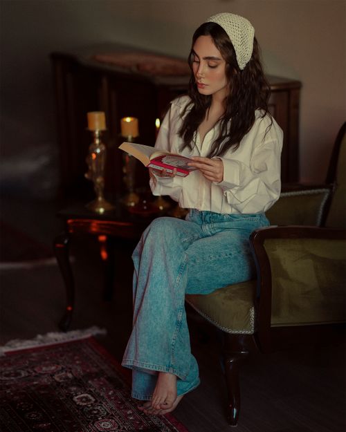 Free A young woman sits comfortably in an armchair reading a book indoors, creating a tranquil and engaging scene. Stock Photo