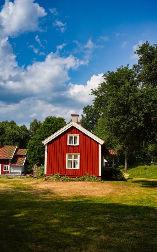 Free A picturesque red house under a blue sky in a peaceful rural landscape. Stock Photo