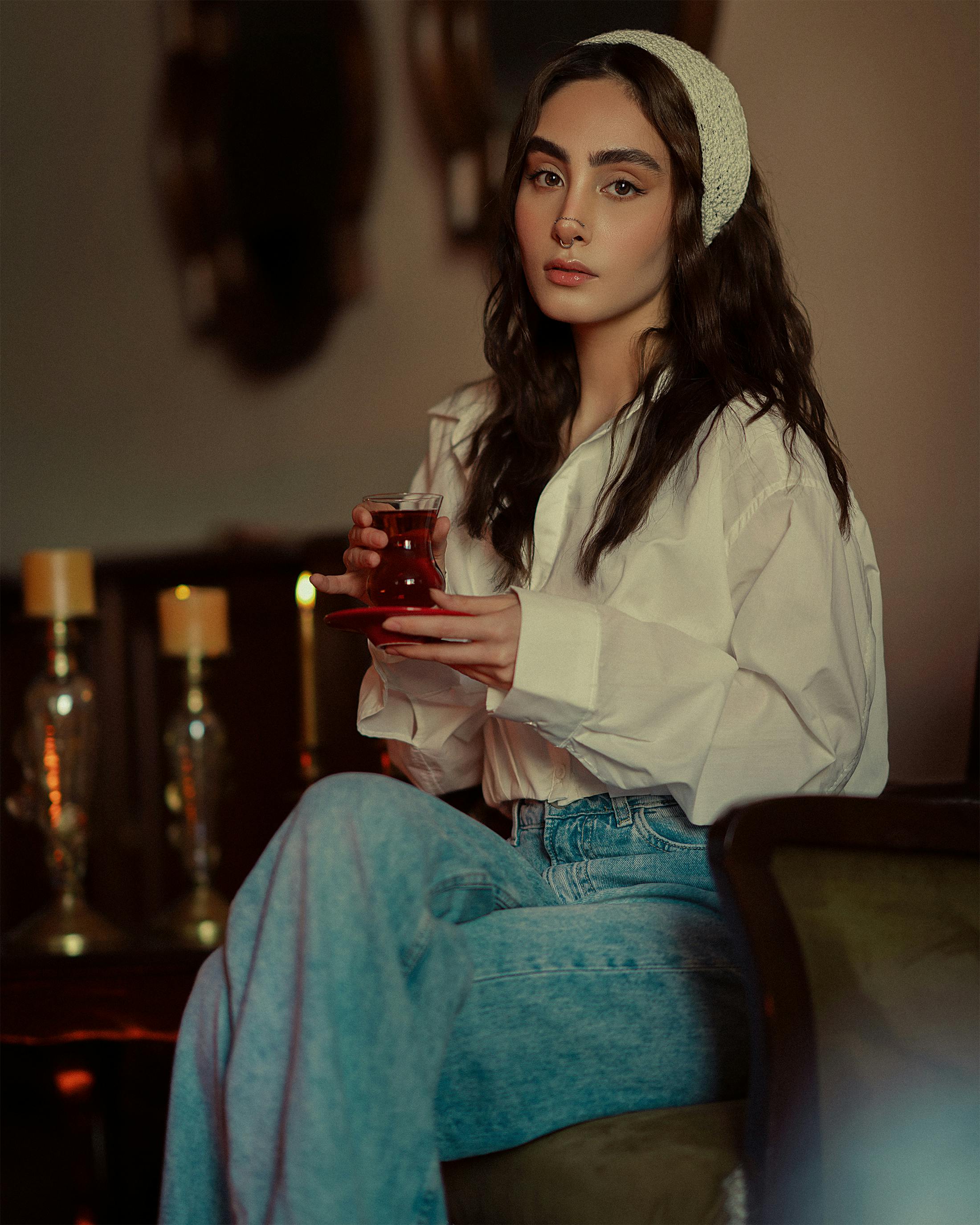 Brunette woman in a white blouse sits elegantly indoors with tea.