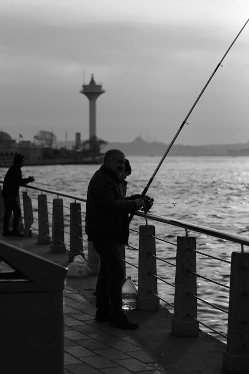 Man Fishing while Standing on the Bridge in City 