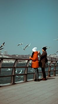 A couple stands on a pier in Istanbul, Turkey, watching seagulls fly over the sea.