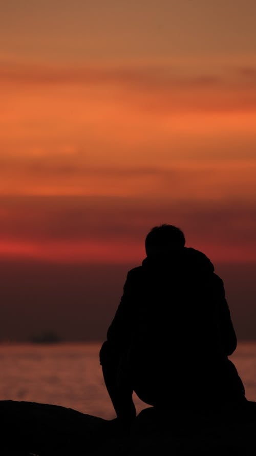 Silhouette of a Man Sitting on the Shore at Sunset 