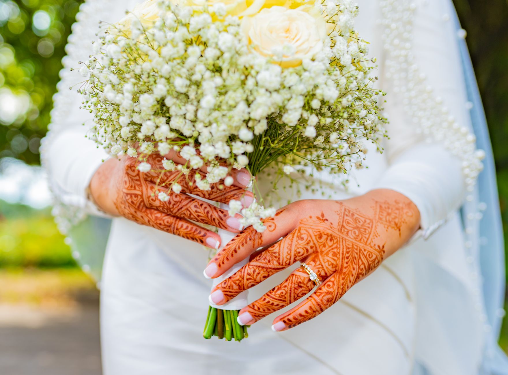 Close-up of a bride holding a bouquet with intricate henna designs on hands.