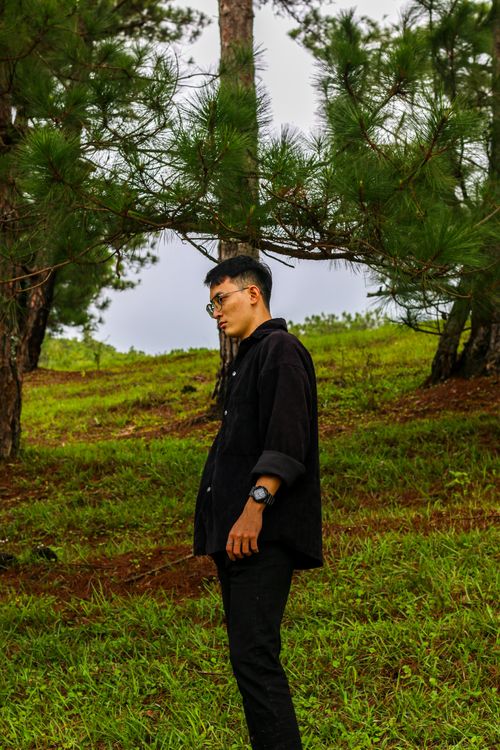 Free A young man in a black outfit stands alone in a lush green park. Stock Photo