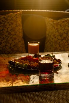 Sun-drenched table with fresh juice, fruit platter, and drinks on a cozy sofa setting.