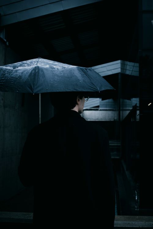 Free Man with umbrella walking through urban street during night rain. Stock Photo