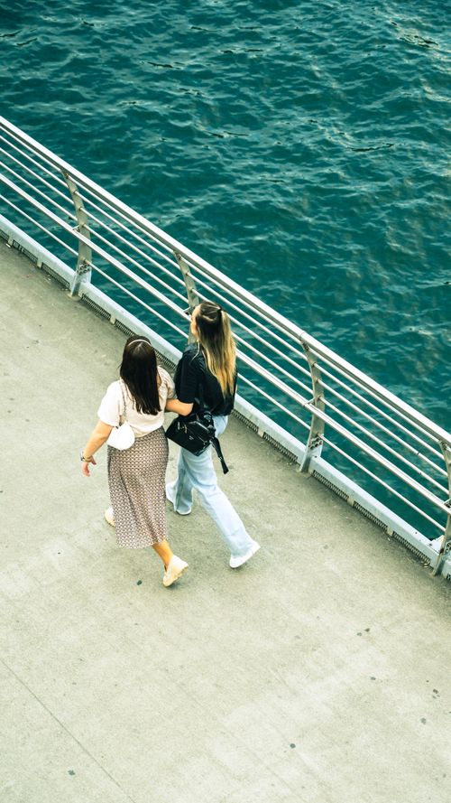 Free Aerial view of two women walking on a pier by the blue sea, enjoying a summer day. Stock Photo