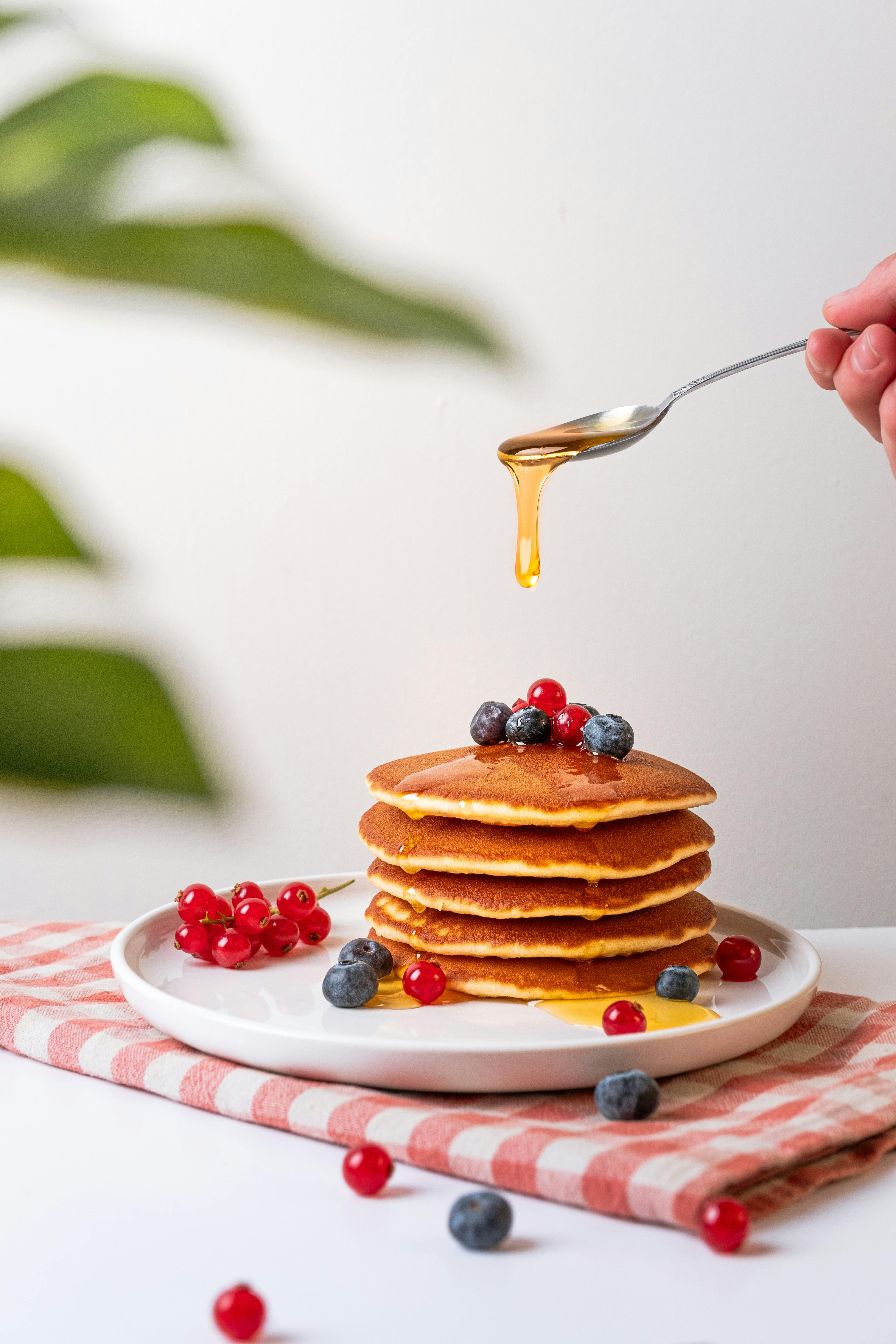 person pouring honey on pancakes with berries