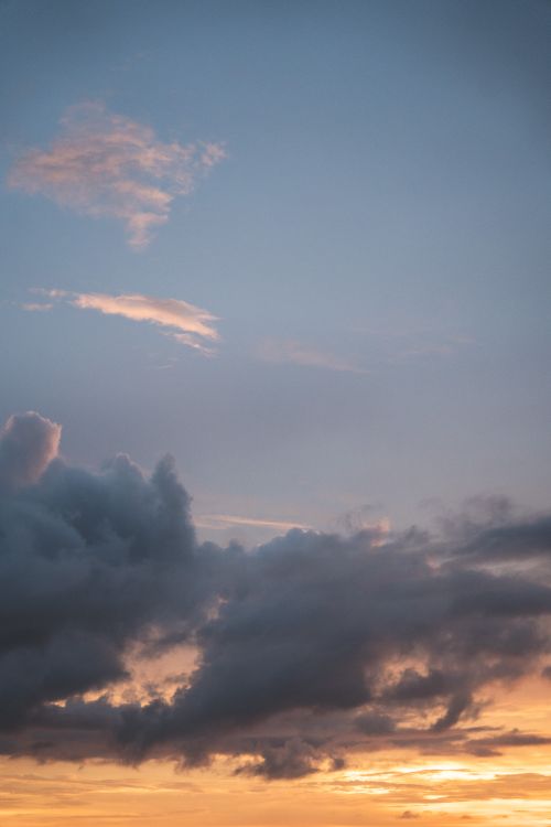Free A tranquil cloudscape at sunset with contrasting dark clouds and warm sky tones. Stock Photo
