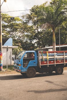 A vibrant blue truck navigates a tree-lined city street, illustrating urban logistics.