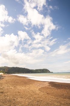 Idyllic beach with lush hills under a bright blue sky in Costa Rica.