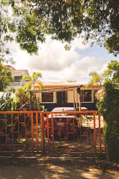 A quaint urban house with red car parked in front, surrounded by lush tropical plants.