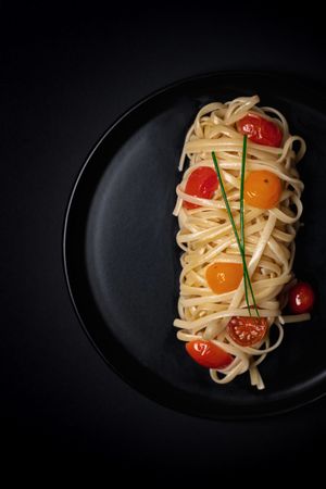 Linguine with cherry tomatoes on a dark plate — photo by Sacha Moreau on Pexels