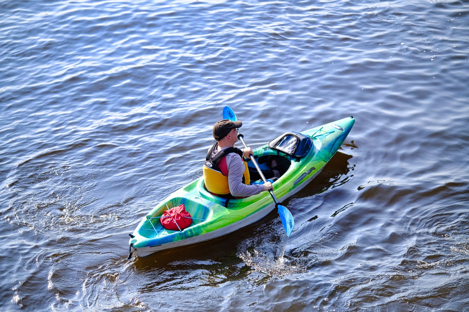 Paddler using a blue kayak on calm water with a visible paddle during an outdoor recreation session