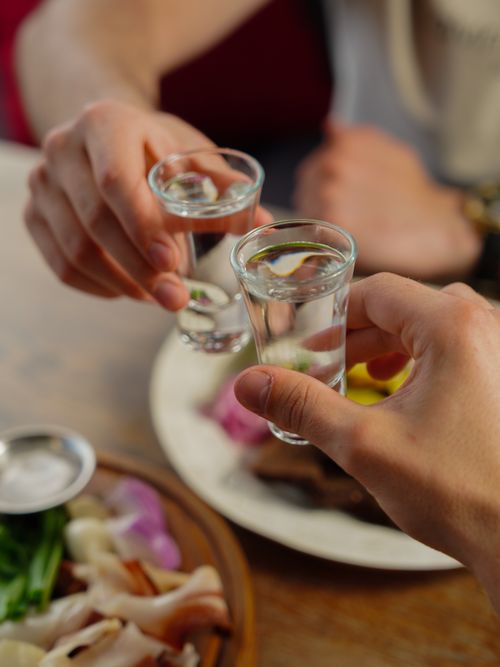 Free Two people clinking shot glasses over a table with appetizers, celebrating together. Stock Photo