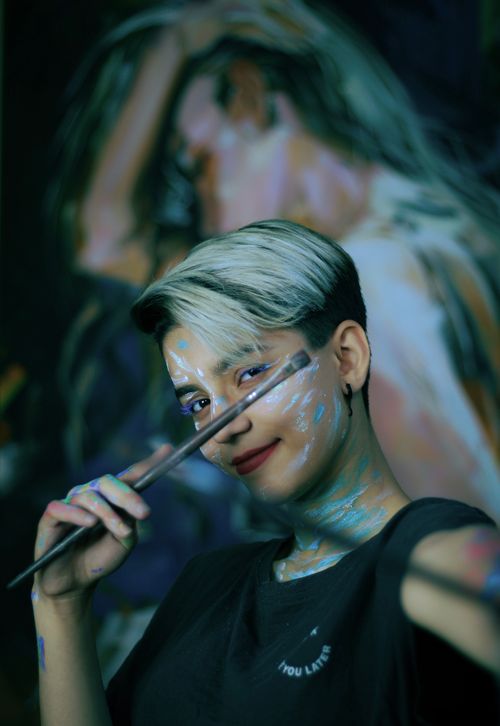 Free Artistic portrait of a woman with short blonde hair, adorned with face paint and holding a paintbrush. Captures creativity and expression. Stock Photo