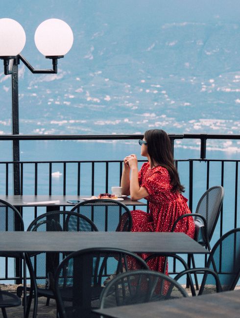 A woman in a red dress sits on a terrace with a scenic sea view.