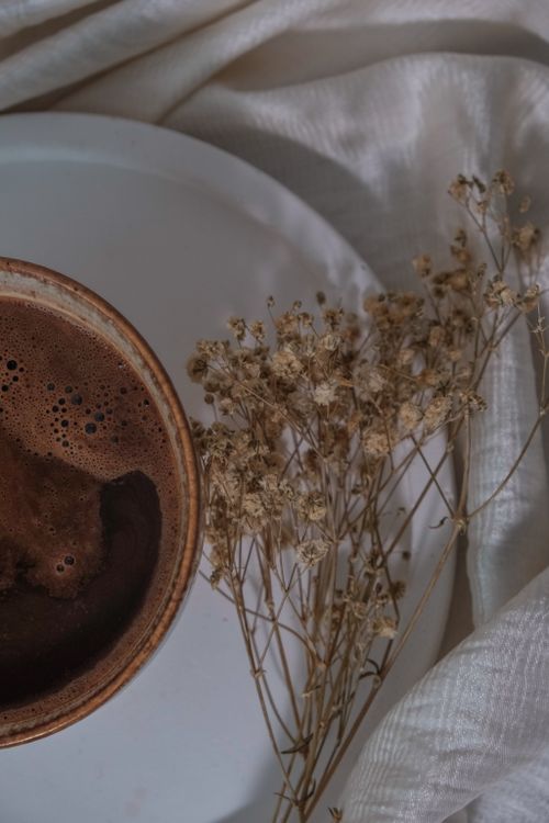 Free Warm coffee cup beside dried flowers on white fabric, creating a cozy atmosphere. Stock Photo