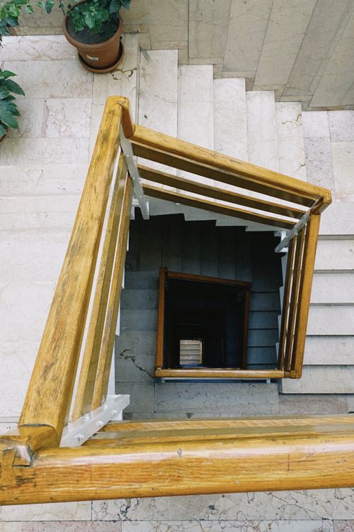 Free Top-down view of a geometric staircase with wooden handrails and marble steps, capturing urban architecture. Stock Photo