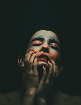 Moody portrait of a woman with colorful face paint, reflecting artistic emotion.