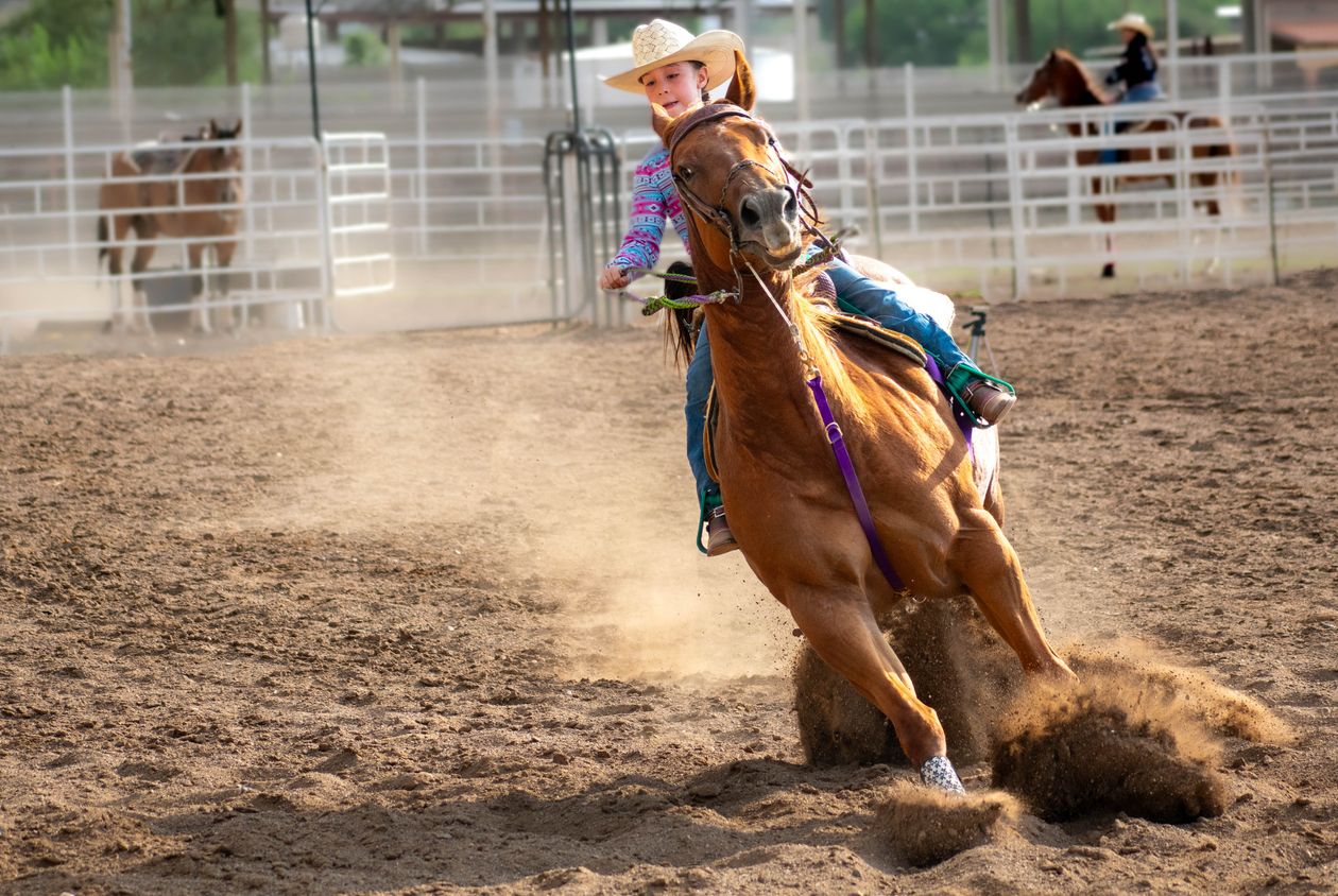 Young rider barrel racing on a chestnut horse, dust flying in the arena