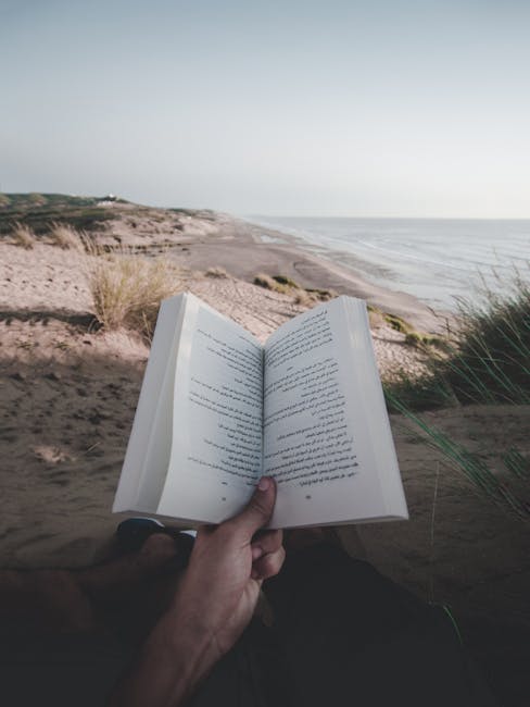A person enjoys reading a book while relaxing on a serene beach, with the ocean in view.