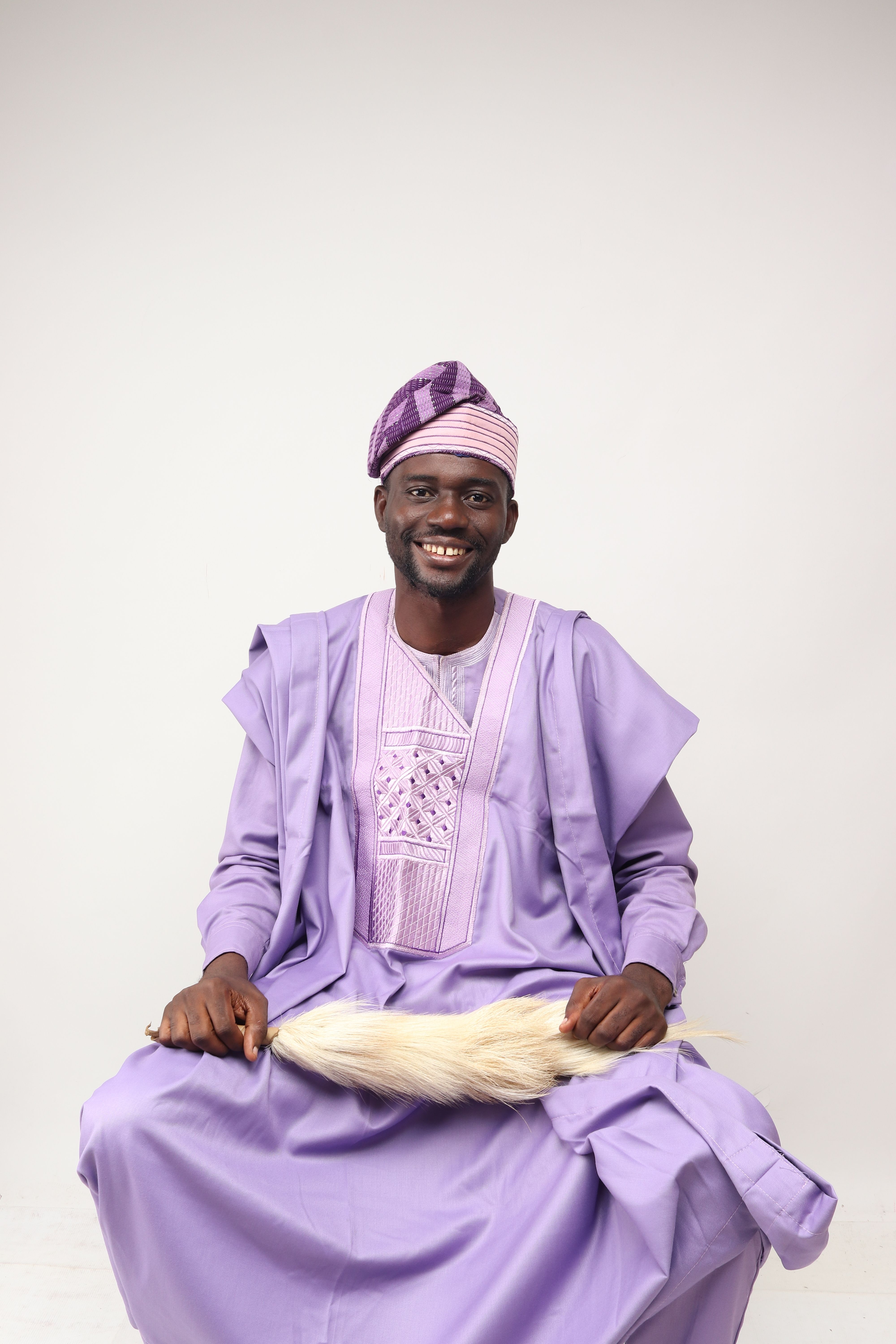 Smiling man in purple traditional attire sitting with a white background.