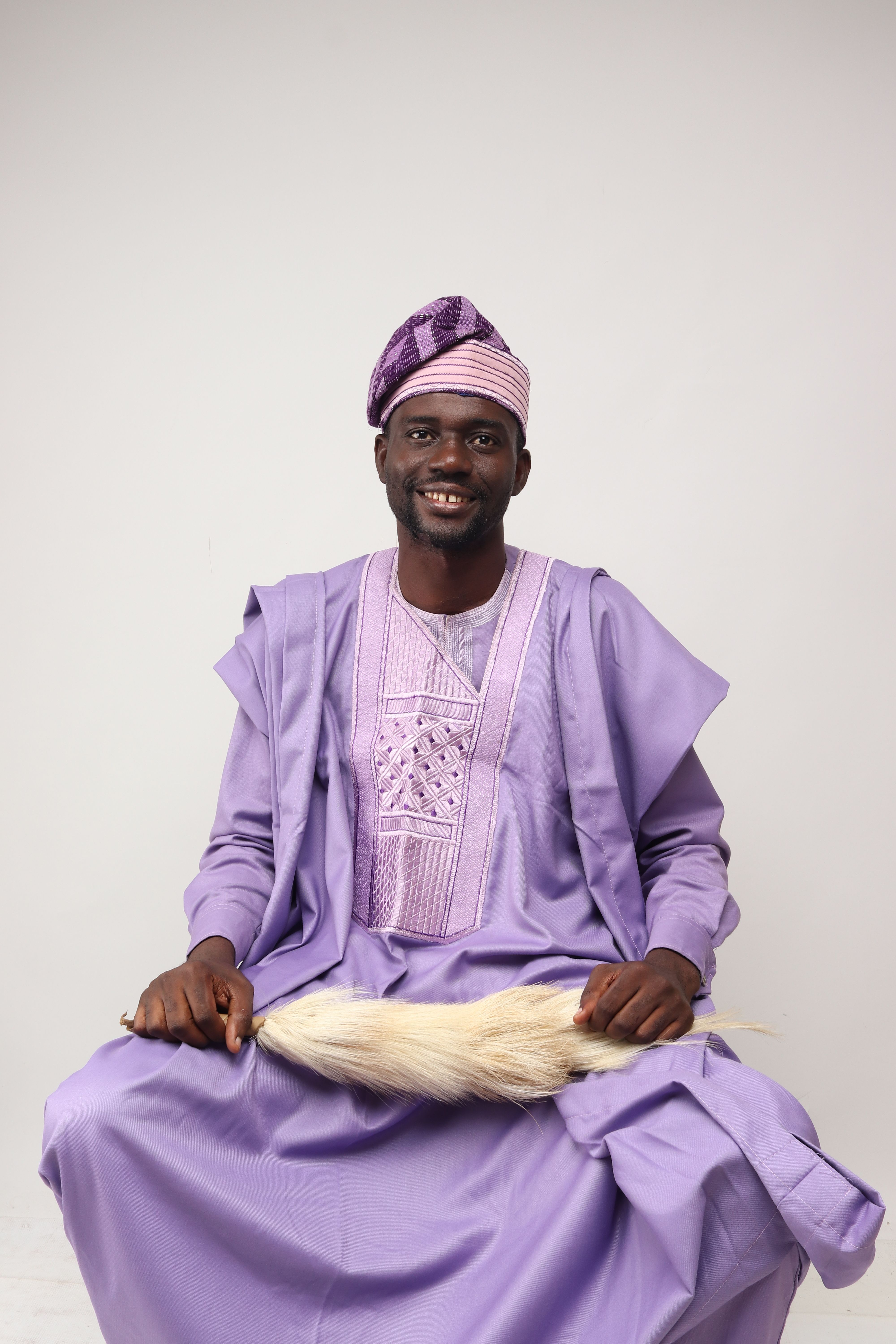 Capture of a smiling man in traditional purple attire posing with a white background.