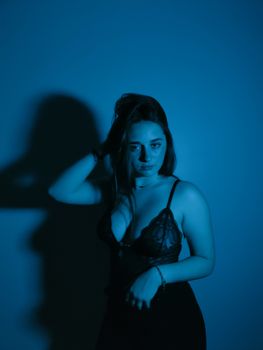 Moody fashion portrait of a woman posing in lingerie against a blue background.