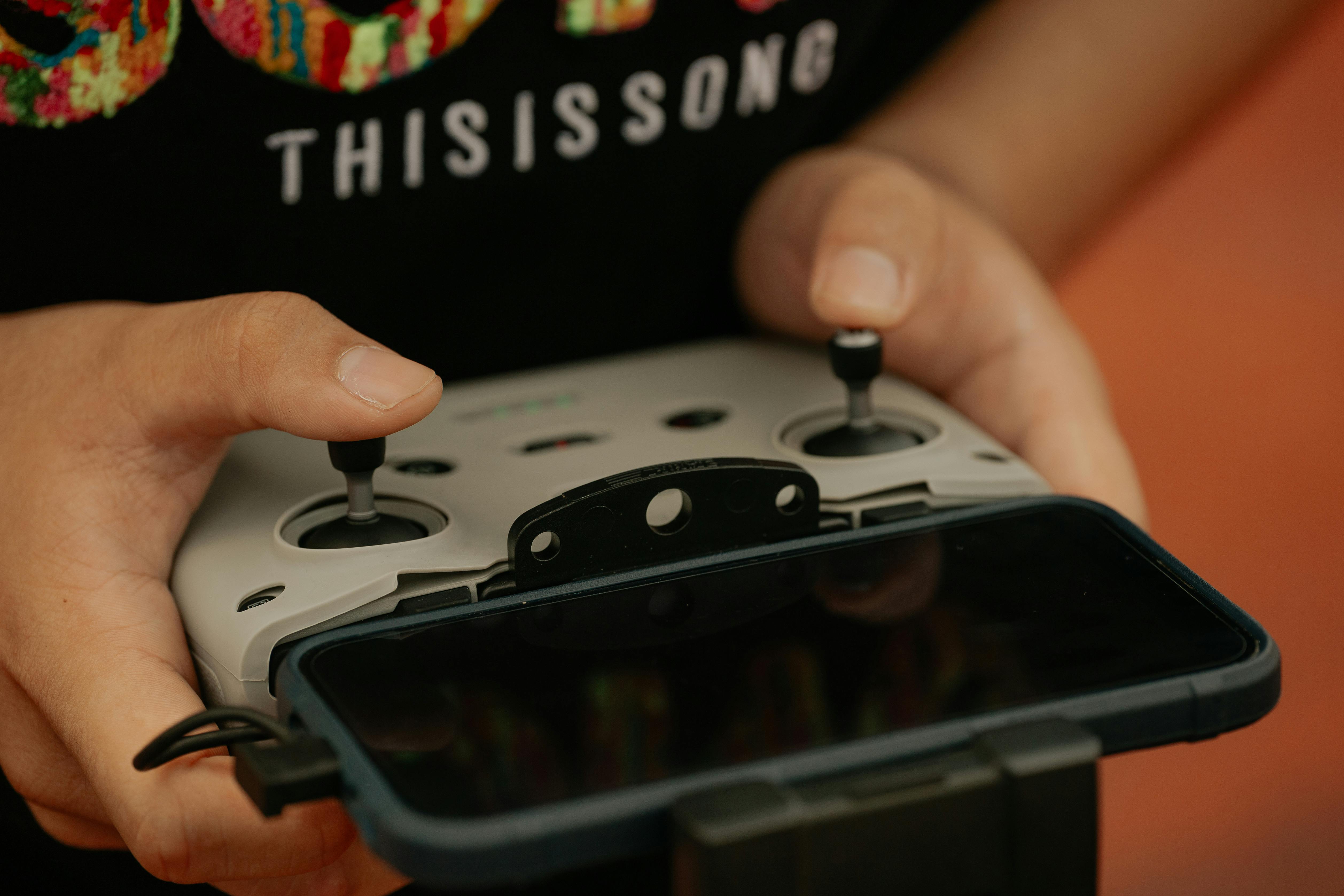 Hands holding a drone controller with a connected mobile device, showcasing modern technology.