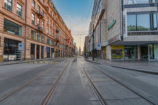 View of an empty street in Prague with shops and tramway tracks at sunset, showcasing urban architecture.