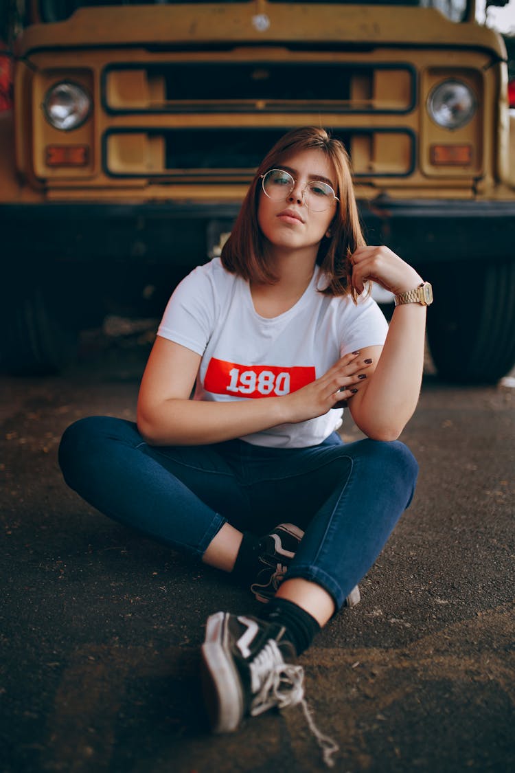 Woman Wearing White T-shirt Sitting On The Ground In Front Of A Yellow Bus