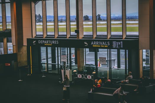 Busy airport terminal area with people, featuring departures and arrivals signs.
