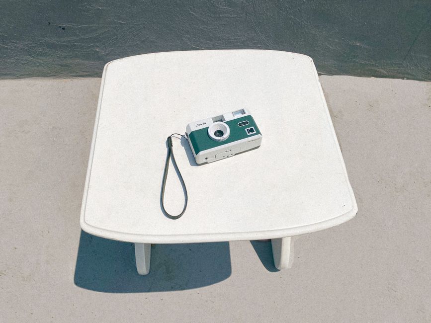 A vintage analog film camera placed on a minimalist white table in an outdoor setting.