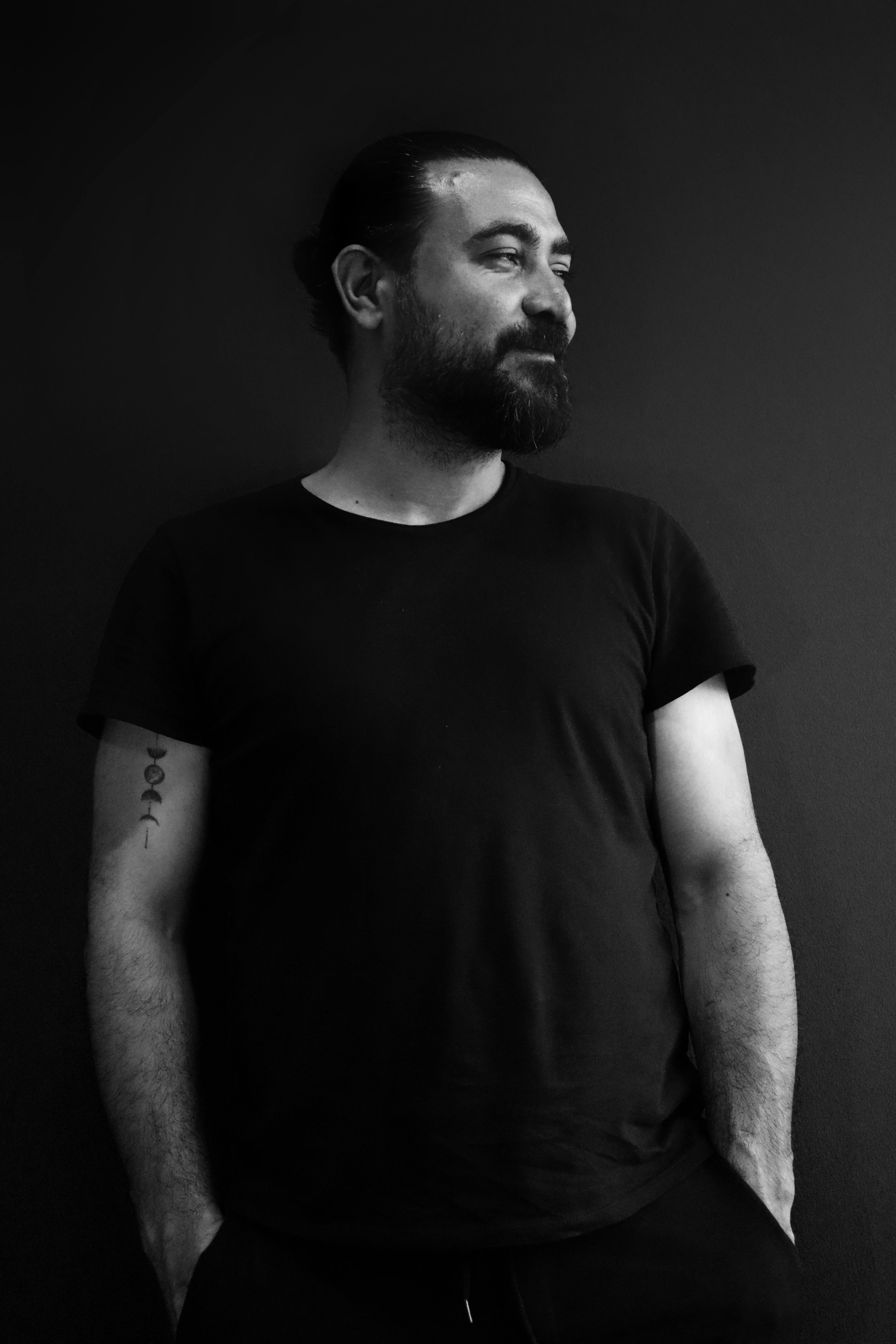 Captivating black and white portrait of a man with a beard and black T-shirt, hands in pockets.